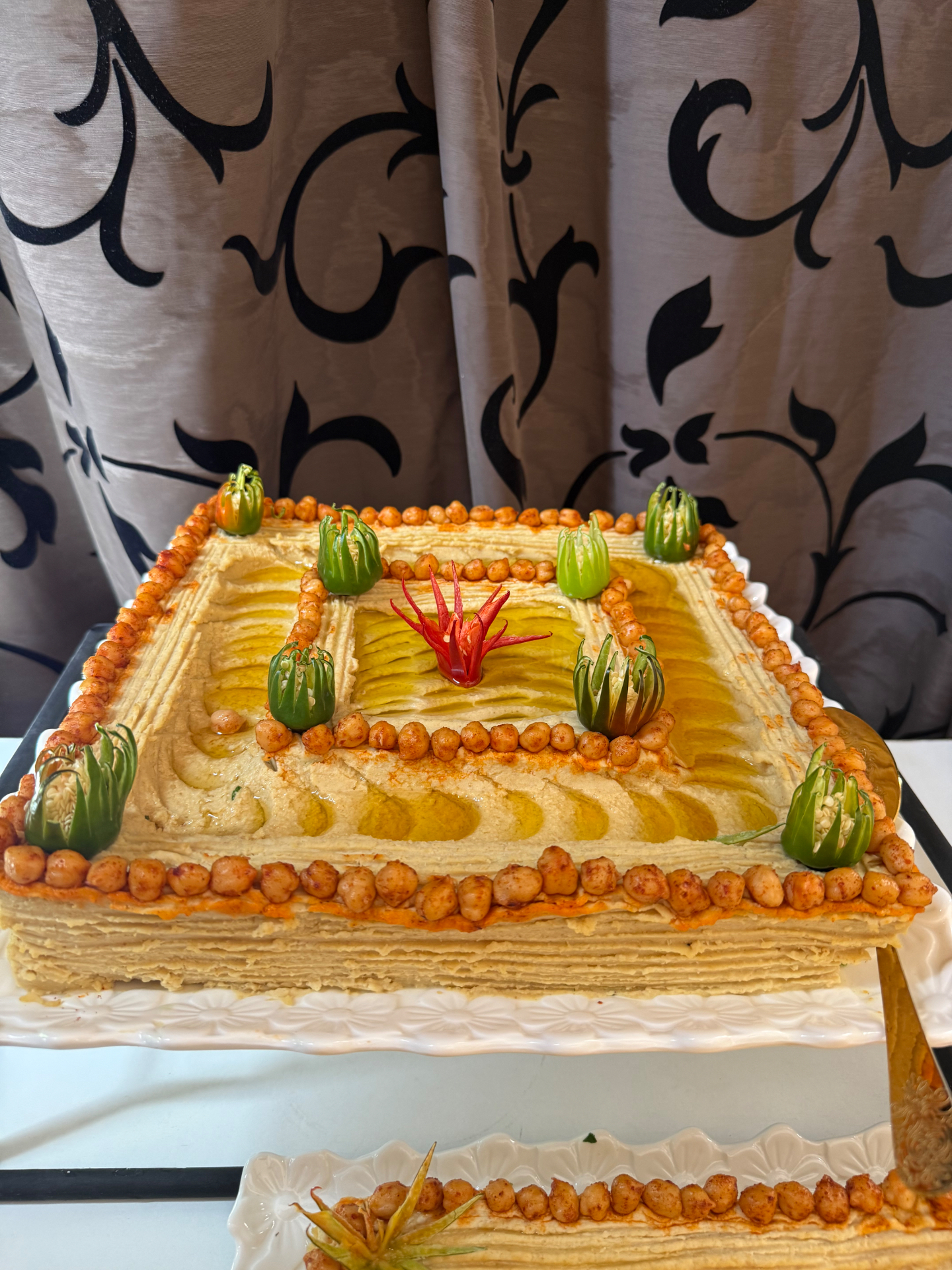 Layered hummus cake decorated with chickpeas and carved peppers